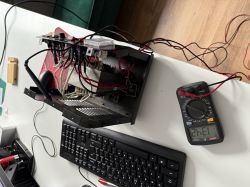 Wnętrze otwartego prostownika z widocznymi przewodami i multimetrem wskazującym napięcie 214,1V.