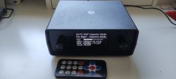 Black radio enclosure with OLED display and IR remote on a tabletop