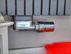 Metalowy zawór zainstalowany na ścianie, z czerwoną plastikową tacą poniżej.