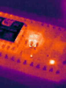 Zbliżenie na zdjęcie termiczne elektroniki z zaznaczoną temperaturą 28°C.