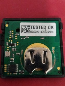 Zbliżenie na płytkę drukowaną z gniazdem na baterię, naklejką TESTED OK oraz komponentami elektronicznymi.