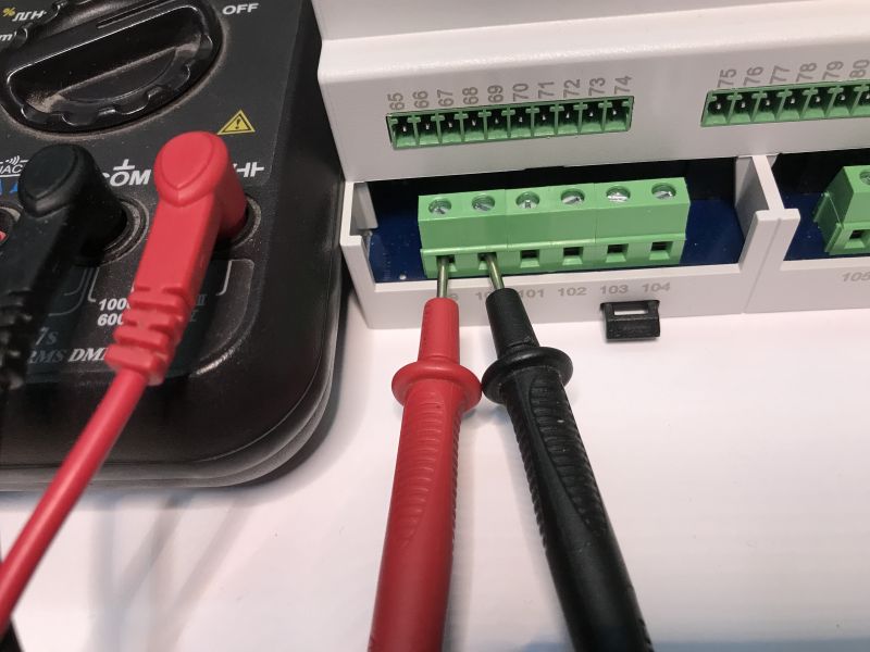 A multimeter with test leads connected to the terminals of an automation device.