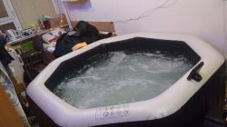 Inflatable hot tub with bubbling water set inside a small room with a bed and window.