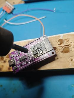 PCB with micro‑USB port and shielded module, pointed at by a soldering iron tip