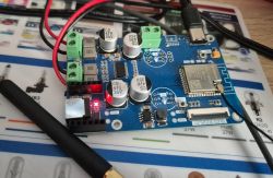 Blue PCB with an ESP32 module, capacitors and terminal blocks, connected via USB cable.