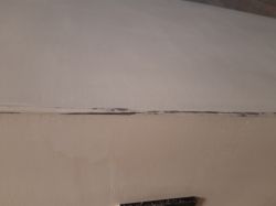 Zbliżenie krawędzi ściany z białą farbą i prześwitującym metalowym narożnikiem