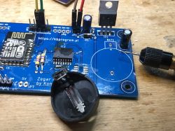 Close-up of a PCB with an ESP8266 module, resistors, and capacitors, and a slot for a clock battery.
