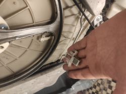 Ręka trzyma plastikowy element z magnesem obok wnętrza pralki.