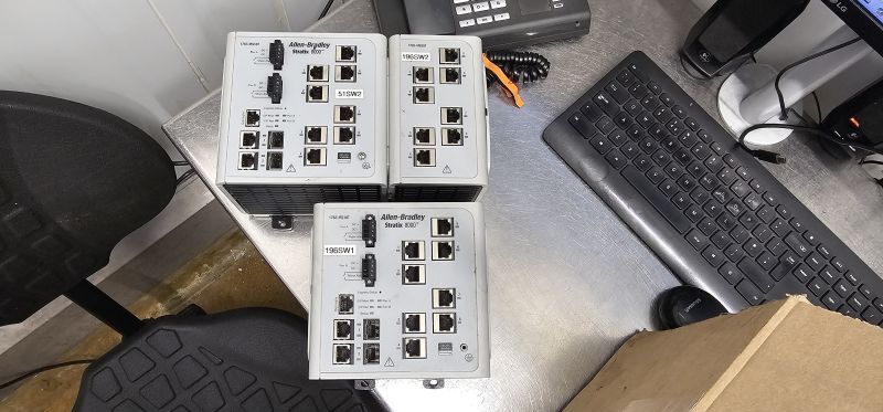 Three Allen‑Bradley Stratix 8000 industrial Ethernet switches on a metal desk beside a keyboard
