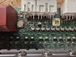 Zbliżenie na fragment płytki drukowanej z elementami elektronicznymi, w tym kondensatorami, rezystorami i złączami.