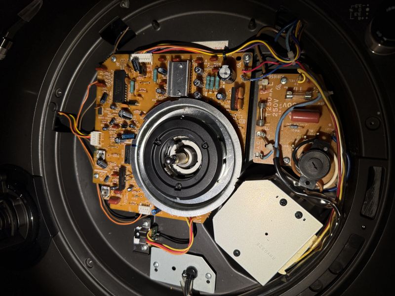 Wnętrze urządzenia z płytką elektroniki, przewodami i centralnym mechanizmem osi