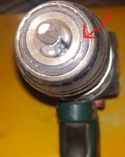 Zbliżenie części metalowej urządzenia z widocznym mechanizmem mocującym, wskazanym czerwoną strzałką.