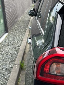 Czarny samochód zaparkowany przy krawężniku obok żwirowego wąskiego pasa.