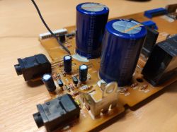 Zbliżenie na płytkę drukowaną z częściami elektronicznymi, takimi jak kondensatory i gniazda, na pomarańczowym tle.