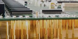 Zbliżenie na płytkę PCB z wystającymi złotymi igłami programatora.
