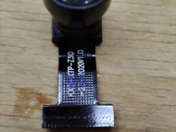 Camera module with flex cable on wooden surface, visible technical markings