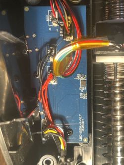 Blue PCB with wires and connectors inside a device; metal spring on the right