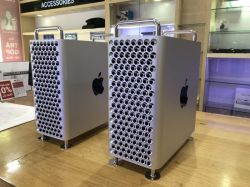 Dwa komputery Apple Mac Pro z perforowanymi panelami stoją na drewnianym blacie w sklepie.