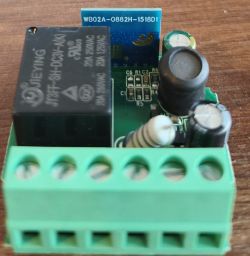 Close-up of a PCB with a relay, capacitors, and a green screw terminal block on a wooden surface