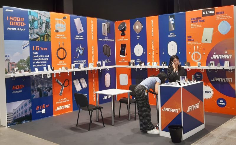 Stoisko wystawowe na targach z elektroniką użytkową, widoczne produkty i reklamy.