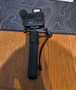 Kamera GoPro zamontowana na uchwycie z lampą LED i mikrofonem, leżąca na drewnianym stole.