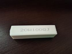 Biały rezystor ceramiczny z nadrukiem 20W100RJ leży na ciemnym blacie.