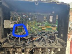 Zbliżenie na wewnętrzną część urządzenia elektronicznego z zaznaczeniem w niebieskim kolorze uszkodzonego obszaru na płytce.