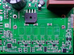 Zbliżenie na zieloną płytkę drukowaną urządzenia elektronicznego z różnymi komponentami, w tym kondensatorem i diodami.