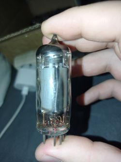 Szklana lampa elektronowa trzymana w ręce z widocznymi pinami i elektrodami wewnątrz.