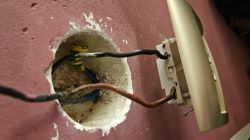 Zbliżenie na niewykończoną puszkę elektryczną w ścianie z widocznymi przewodami: czarnym, brązowym i niebieskim.