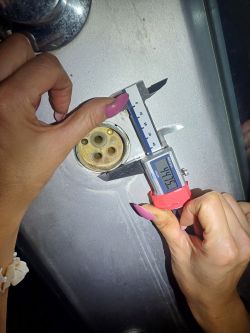Hands using a caliper to measure a component in a sink.