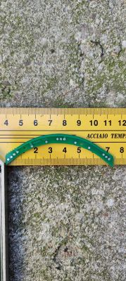 Złamany zielony fragment obwodu drukowanego obok żółtej linijki na tle chropowatej powierzchni.