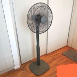 Panasonic standing electric fan on a wooden floor in a bright room.