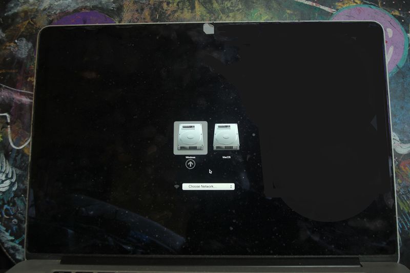 MacBook screen with startup disk selection: Windows and MacOS icons and a Wi‑Fi network dropdown.