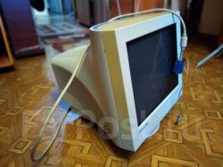 Stary monitor CRT Samsung na parkiecie, z przewodem VGA i białym kablem przerzuconymi przez obudowę.