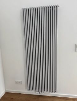 Dekoracyjny grzejnik Tubes 25 Basic przymocowany do ściany salonu.