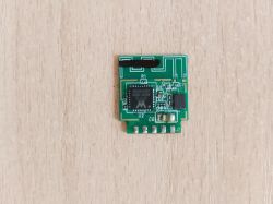 Small green circuit board with an electronic chip on a wooden surface.