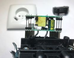 Inside a USB wall socket: two PCB boards with a transformer and capacitor, with a white faceplate in back
