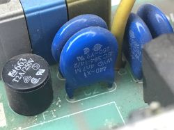 Zbliżenie płytki PCB z niebieskimi warystorami i czarnym kondensatorem oznaczonym „T2A/250V”