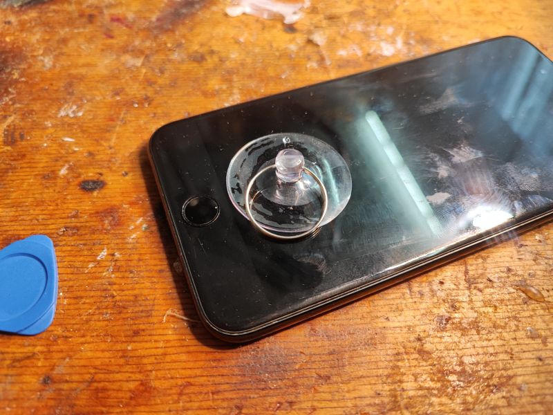 iPhone Screen Removal Using Suction Cup and Guitar Pick Phone with suction cup on the screen and a guitar pick lies on a table.