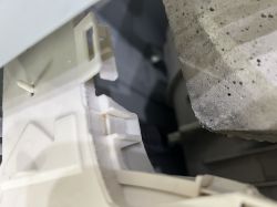 Fragment wnętrza pralki Hotpoint z plastikowym elementem i amortyzatorem.