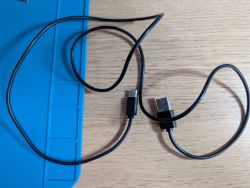 Black USB-A to USB-C cable on wooden surface next to blue mat