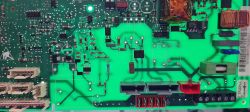 Zbliżenie na zieloną płytkę drukowaną z widocznymi złączami, cewkami i komponentami elektronicznymi.