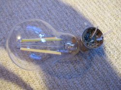 A broken LED bulb lying on a light-colored carpet.