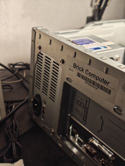Tył obudowy komputera z kratką wentylacyjną zasilacza i naklejką „Brick Computer”