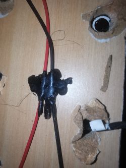 Czarne i czerwone przewody elektryczne połączone substancją klejącą, przytwierdzone do drewnianej powierzchni z otworami.