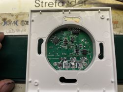 Printed circuit board with electronic components inside a plastic housing, likely a wall thermostat.