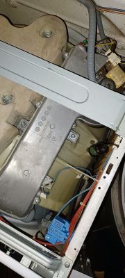 Wnętrze pralki z widocznymi elementami mechanicznymi i rurkami.