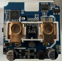 Close-up of a PCB with surface-mount chips and two gold battery contacts in a white holder