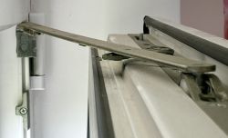 Zbliżenie na mechanizm okna uchylnego ukazujący metalowe zawiasy.